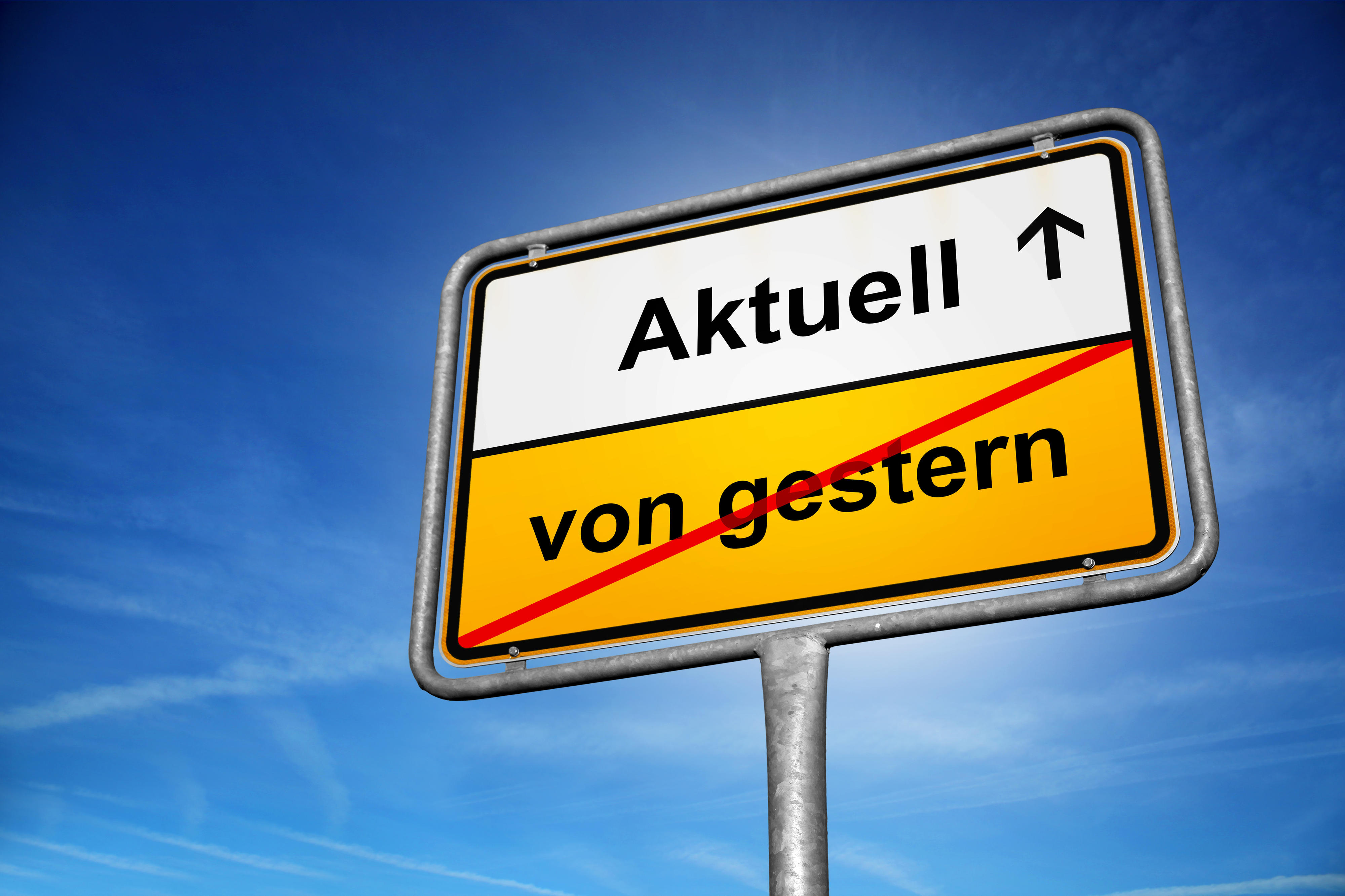 Außerorts-Verkehrsschild: Oben "Aktuell", unten durchgestrichen "von gestern", vor blauem Himmel.