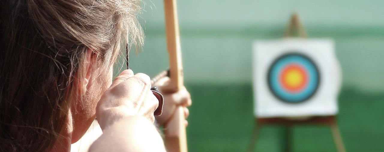 Frau zielt mit einem Bogen auf eine Zielscheibe
