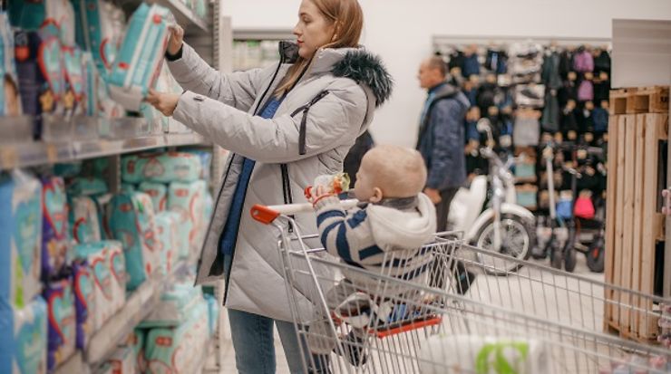 Frau steht vor einem Regal mit Windeln und greift nach Packung