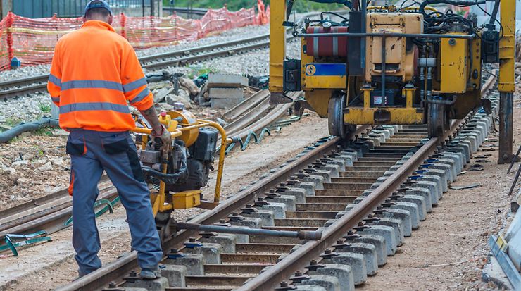 Ein Mann arbeitet mit einer Maschine an Bahngleisen