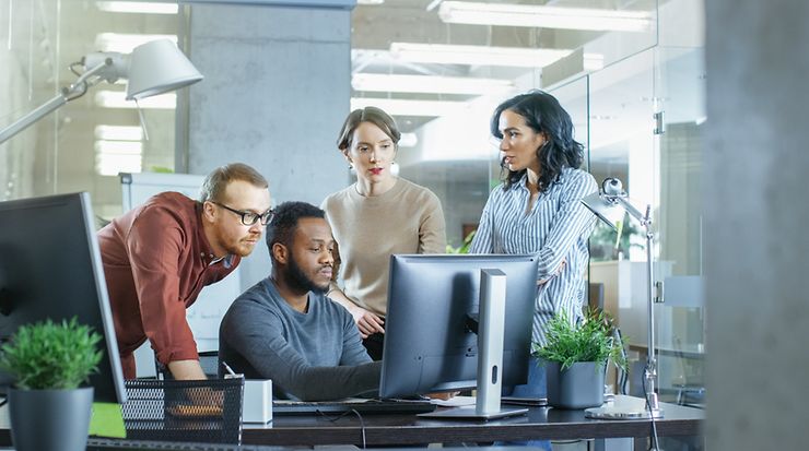 Personen um einen Arbeitsplatz, die gemeinsam auf einen Bildschirm schauen