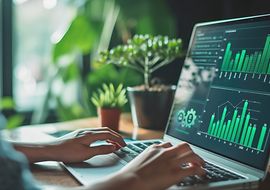 Person arbeitet am Laptop mit grünen Datenvisualisierungen, Pflanzen im Hintergrund.
