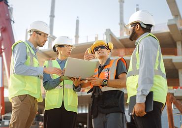 Baufachleute besprechen sich auf einer Baustelle und schauen auf ein Tablet