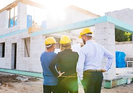 Drei Personen schauen auf einen Bauplan auf einer Baustelle