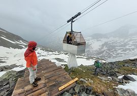 Personen bei der Beladung einer Materialseilbahn in verschneiter Berglandschaft