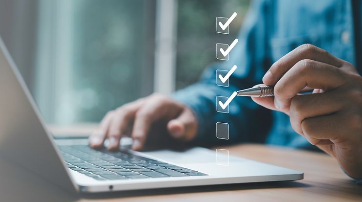 Person arbeitet am Laptop, hakt digitale Checkboxen ab; symbolisiert Planung und Organisation.