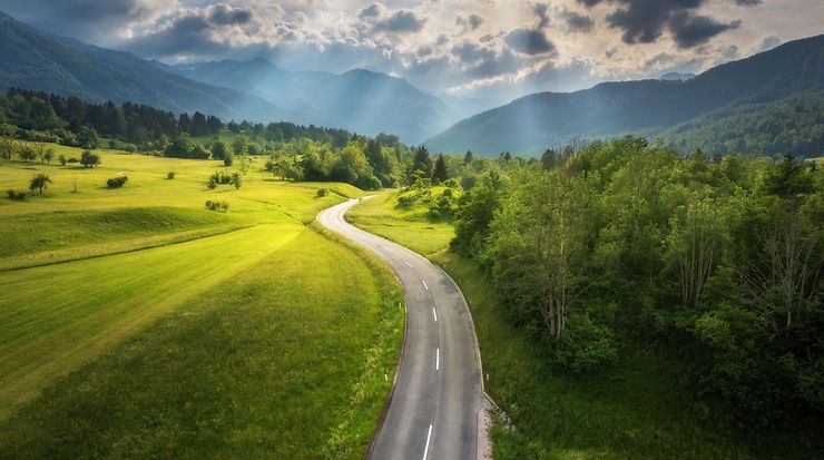 Luftaufnahme einer Straße in einer grünen Wiese bei Sonnenuntergang im Sommer.