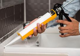 Person verwendet Silikonpistole zur Abdichtung eines Waschbeckens