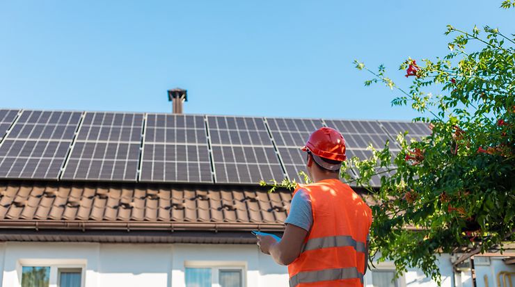 Mann in orangener Weste bewerten Solaranlage auf einem Dach