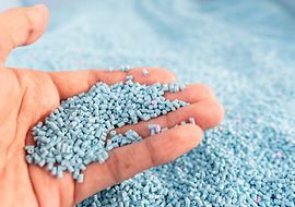 Ein Hand hält hellblaues Kunststoffgranulat ins Bild