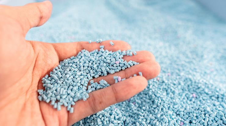 Ein Hand hält hellblaues Kunststoffgranulat ins Bild