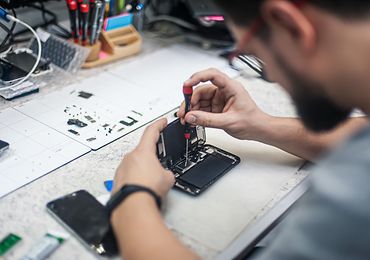 Blick über die Schulter einer Person, die an einem Smartphone schraubt und es repariert