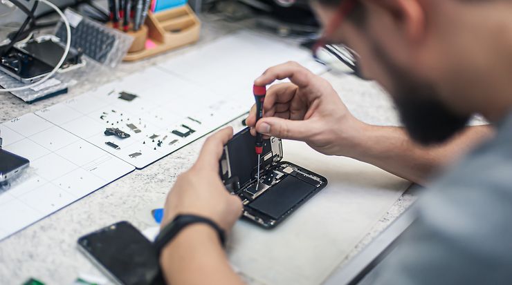 Blick über die Schulter einer Person, die an einem Smartphone schraubt und es repariert