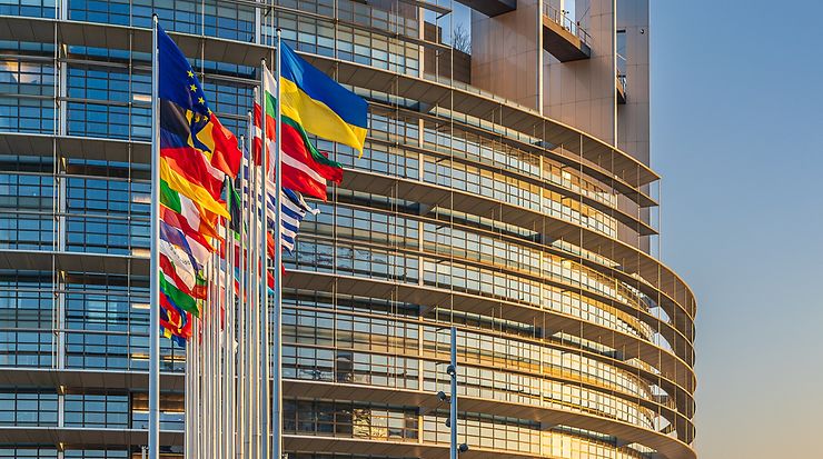 Flaggen von EU-Mitgliedsstaaten vor einem modernen Gebäude bei Sonnenuntergang