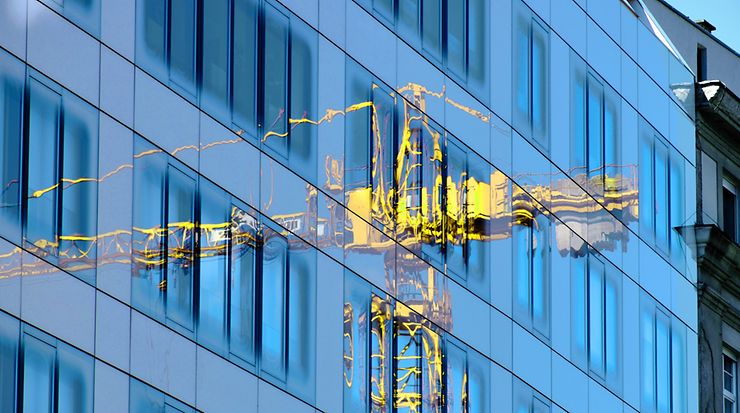 Ein gelber Baukrahn spiegelt sich in einer verglasten Fassade