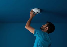 Person installiert Rauchmelder an der Decke.