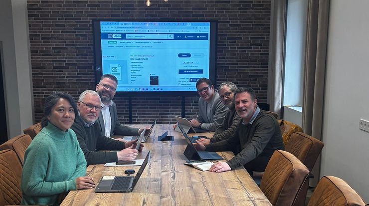 Gruppe von Personen in Besprechung mit Laptops, Präsentation auf Bildschirm.