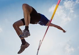 Ein Stabhochspringer überquert die Latte vor blauem Himmel.