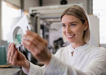 Frau schaut ein Maschinenbauteil an und prüft dieses