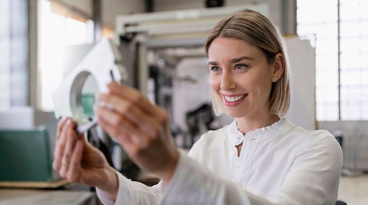 Frau schaut ein Maschinenbauteil an und prüft dieses