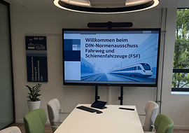 Moderner Konferenzraum des DIN-FSF mit Bildschirm und grünen Stühlen.