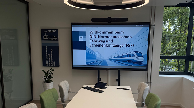 Moderner Konferenzraum des DIN-FSF mit Bildschirm und grünen Stühlen.