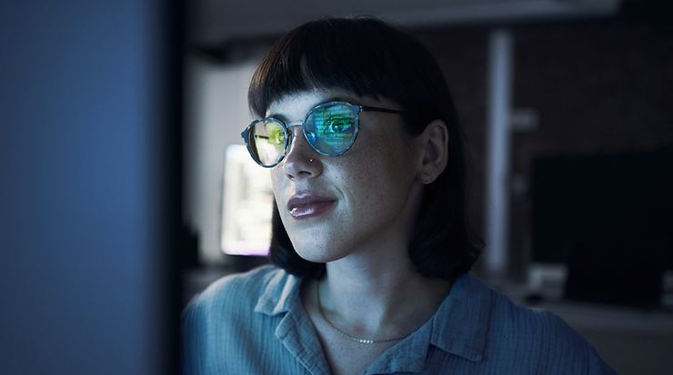 Frau, die auf ein Bildschirm schaut und in ihrer Brille spiegelt sich der Bildschirm