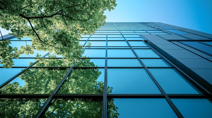 Spiegelnde Glasfassade eines Gebäudes mit Baum und Himmel im Reflexion.
