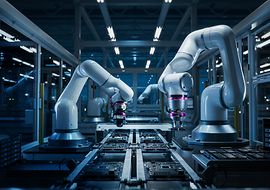 Zwei große, weiße industrielle Roboterarme in einer modernen, automatisierten Fertigungseinrichtung. 