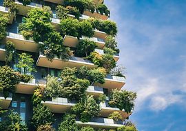 Grüne Fassade eines modernen Gebäudes mit üppiger Bepflanzung auf Balkonen vor blauem Himmel.