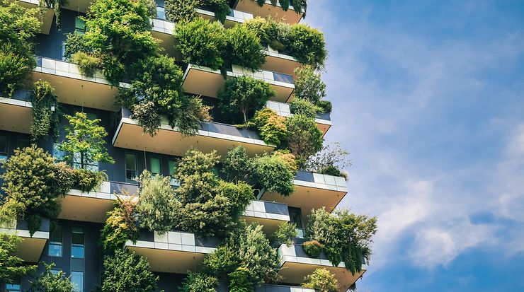 Grüne Fassade eines modernen Gebäudes mit üppiger Bepflanzung auf Balkonen vor blauem Himmel.
