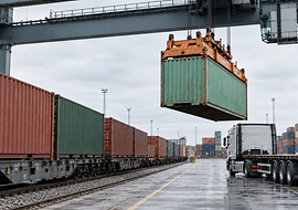 Ein Kran hebt einen Container zwischen Güterzug und Lkw in einem Umschlagterminal