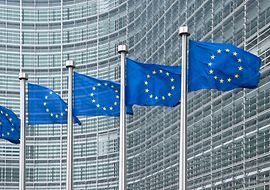 EU-Flaggen vor moderner Glasfassade eines EU-Gebäudes.