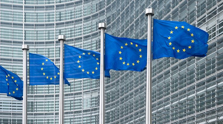 EU-Flaggen vor moderner Glasfassade eines EU-Gebäudes.