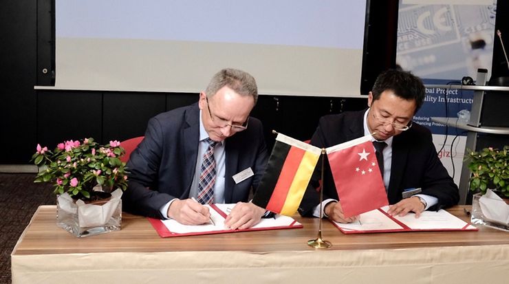 Volker Jacumeit und Mr. Liu Xiangang unterschreiben eine Vereinbarung. Eien deutsche und chinesiche Flagge stehen auf dem Tisch.