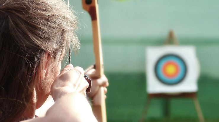 Frau zielt mit einem Bogen auf eine Zielscheibe