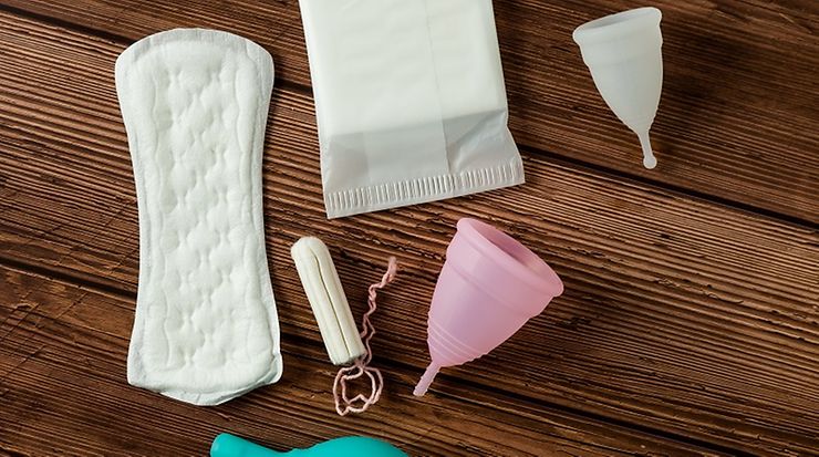 Verschiedene Menstruationsprodukte auf Holzuntergrund, inklusive Binden und Menstruationstassen.