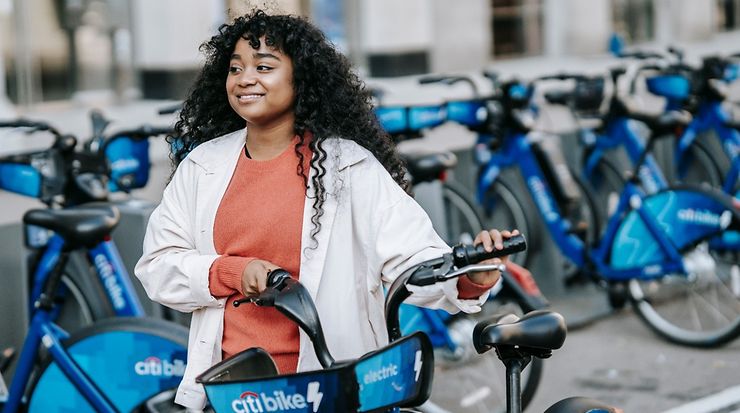 Frau mit Verleih-Fahrrad bei einem typischen städtischen Fahrradverleihpunkt